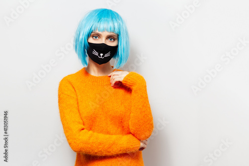 Studio portrait of young girl with blue bob hairstyle, wearing orange sweater and medical mask against coronavirus or covid-19. Background of white.