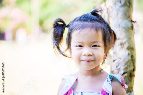 Adorable Asian little girl with a sweet smile looking at the camera. Happy child in the grass during summer or spring. Happy in the summertime. Kid is 3 years old.