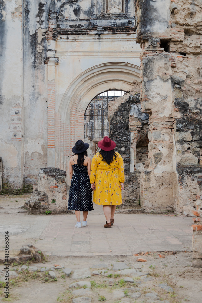 Friends walking through ruins of the Santiago Cathedral in Antigua Guatemala - two friends on vacation in colonial city - tourists discovering new places