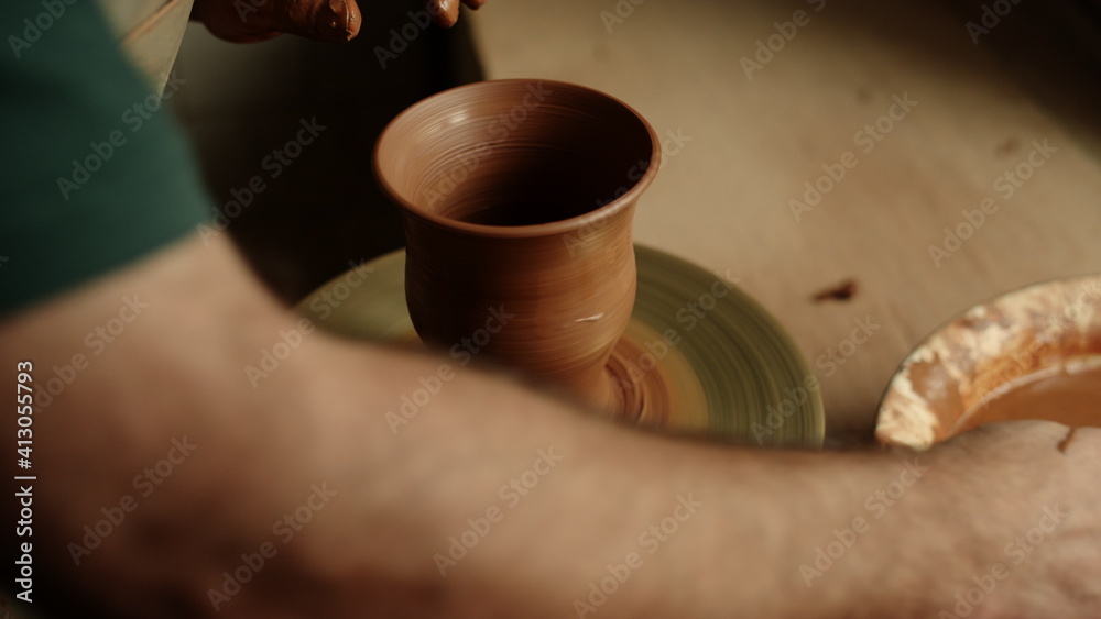 Ceramist modeling clay jar in pottery. Guy cleaning potters wheel with