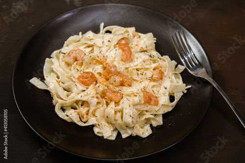 Delicious Italian pasta. Fetuccini with shrimp and herb sauce on black plate and dark background.
