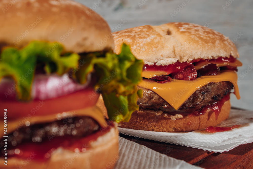 Delicious burgers with Bacon and cheddar cheese and with lettuce, tomato and red onion and bacon on homemade bread with seeds and ketchup. Focus in second burguer. Delicious burgers with Bacon and cheddar cheese and with lettuce, tomato and red onion and bacon on homemade bread with seeds and ketchup. Focus in second burguer.