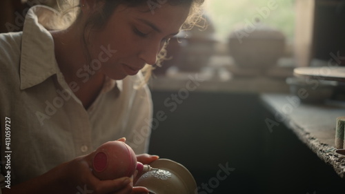 Excited lady doing handicraft on clay product in pottery. Woman drawing ornament