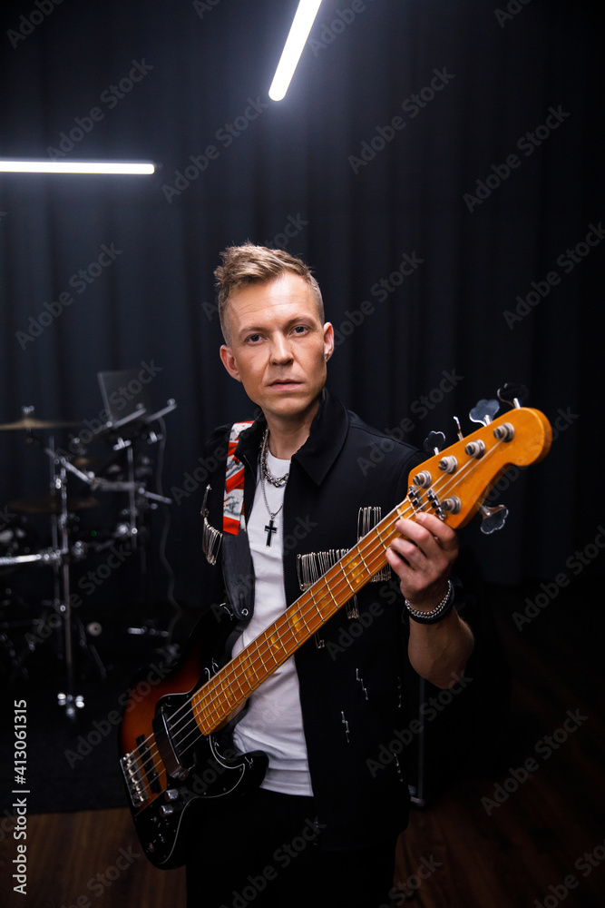 Obraz premium brutal portrait of a man musician in black clothes against the background of musical instruments holding a guitar in his hands