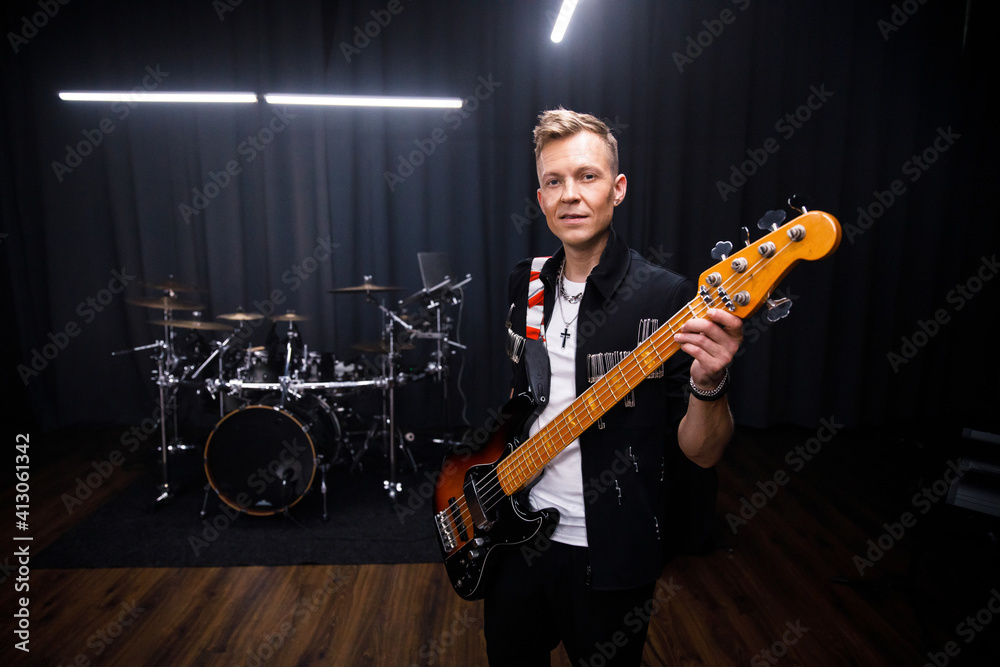 Fototapeta premium brutal portrait of a man musician in black clothes against the background of musical instruments holding a guitar in his hands