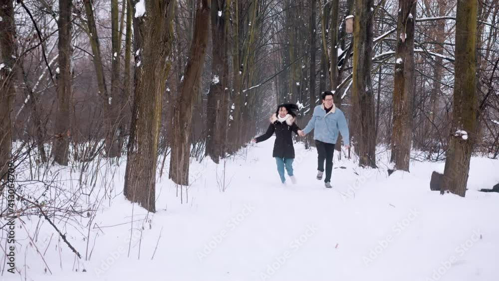 Happy couple running through the park covererd in snow and holding hands. Slow motion. High quality 4k footage Happy couple running through the park covererd in snow and holding hands. Slow motion. High quality 4k footage