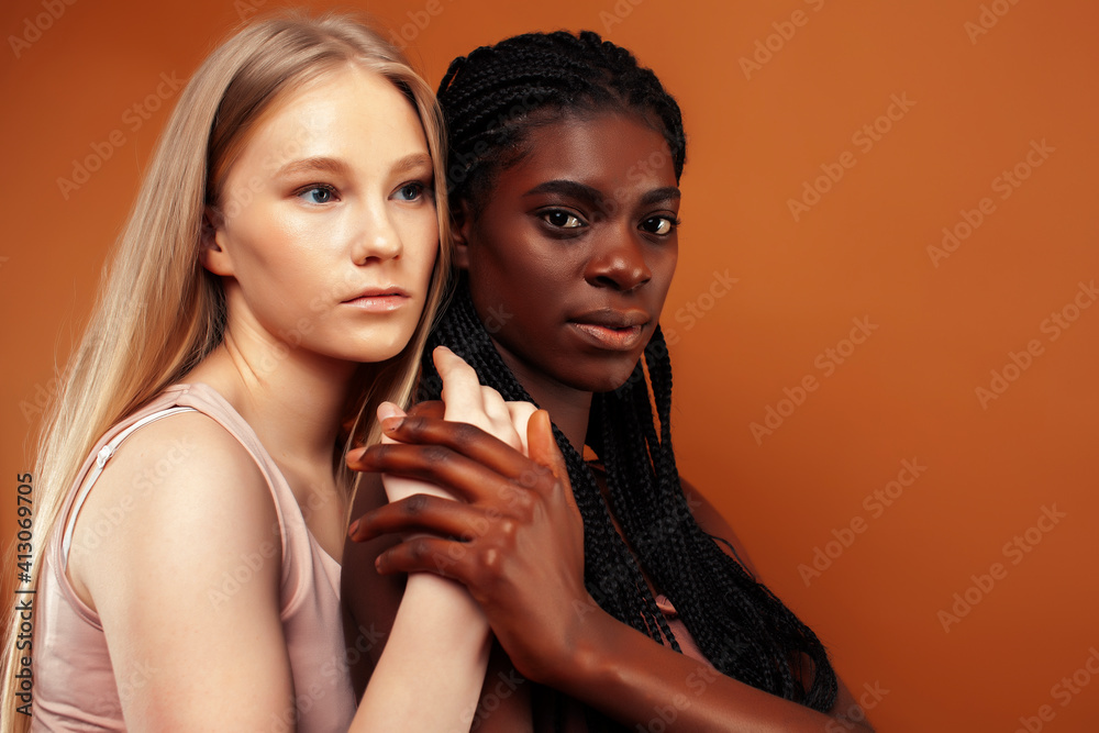 two pretty girls african and caucasian blond posing cheerful together on brown background, ethnicity diverse lifestyle people concept