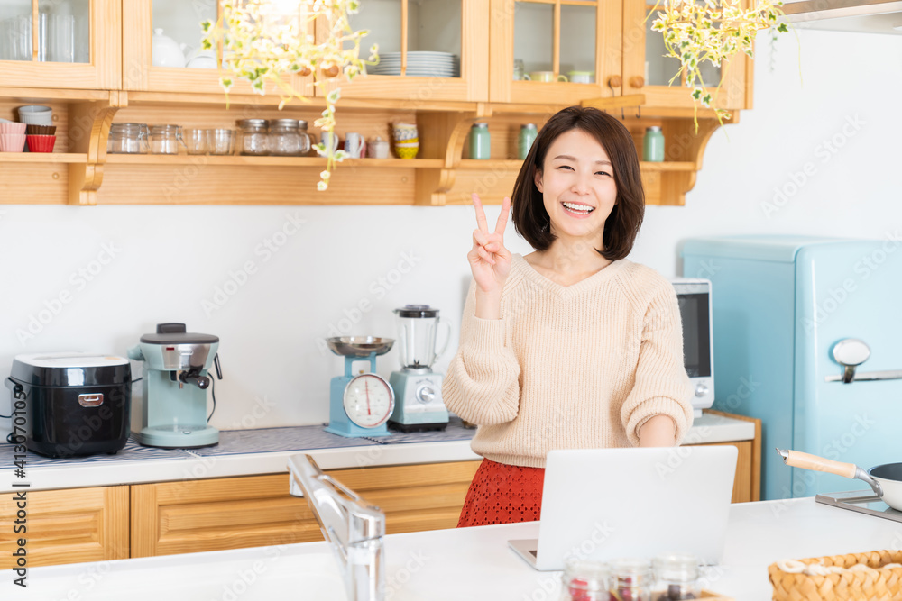 キッチンでラップトップコンピューターを見る女性 キッチンでラップトップコンピューターを見る女性