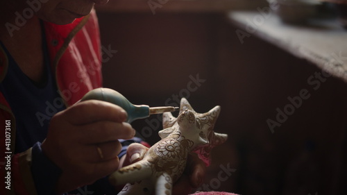 Elderly woman putting dots on product in pottery. Lady decorating toy moose