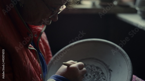 Elderly woman making ornament on product in pottery. Lady scraping in studio