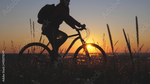 The silhouette of cyclist traveler rides along the edge of the mountain, admiring the landscape and the sunrise. Free tourist rides a bike in nature in the sun. Sports lifestyle. Cyclist exercising