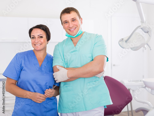 Portrait of adult smiling dentist in medical center with assistant