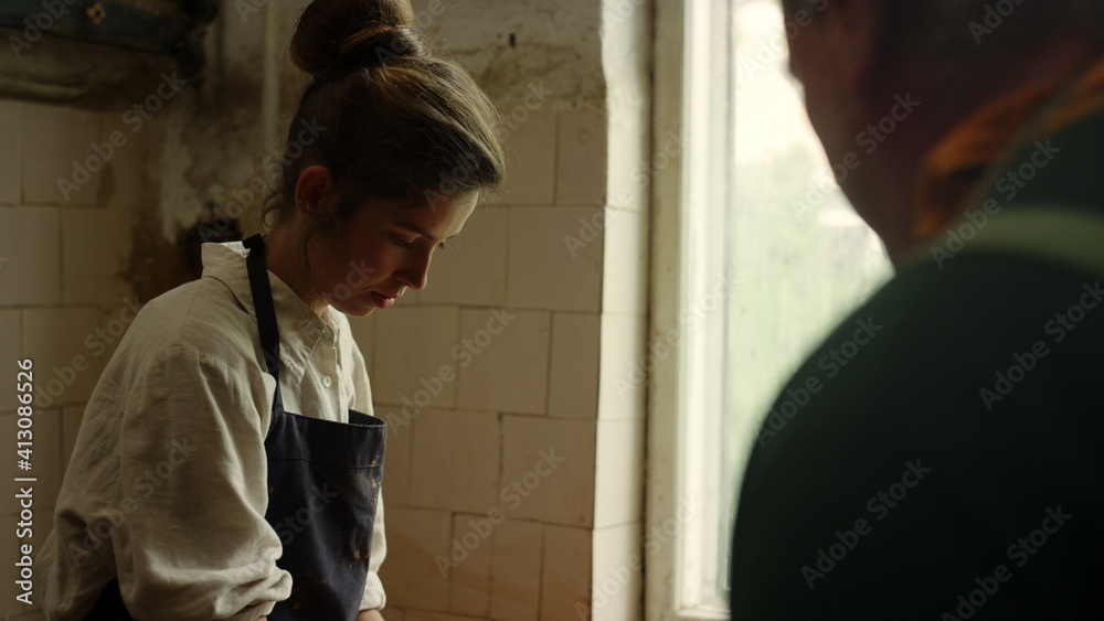 Man giving master class to girl in pottery. Lady working with potters wheel