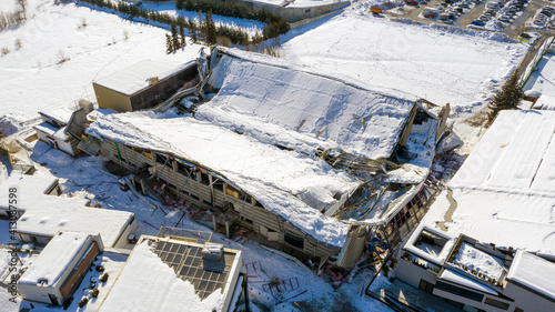 The roof collapsed under the weight of snow. Aerial view of damaged falling roof inside a publica city area. Large collapsed condominium or industrial company. View from above with a drone.