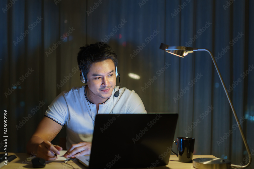 Asian man work at home are sitting at work with colleagues or managers via video call at night at home.. Asian man work at home are sitting at work with colleagues or managers via video call at night at home..