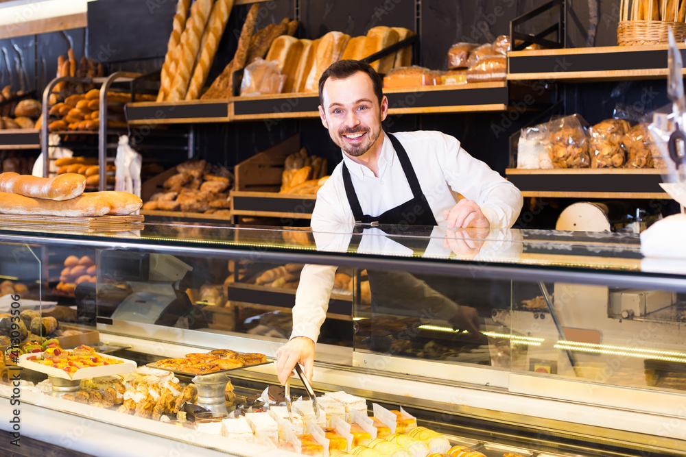 Smiling confectioner showing range of cakes at a bakery