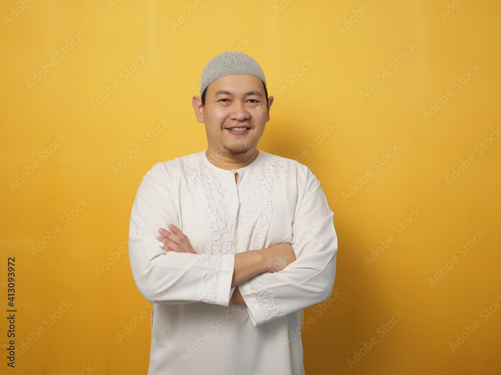 Portrait of Asian muslim man smiling friendly with crossed arms, confident gesture, successful businessman, against yellow Portrait of Asian muslim man smiling friendly with crossed arms, confident gesture, successful businessman, against yellow