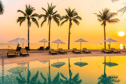 Fototapeta Naklejka Na Ścianę i Meble -  Umbrella and chair around outdoor swimming pool with sea beach ocean at sunset
