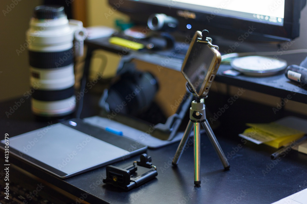 Naklejka premium A person's hand holding a pen and using a graphic tablet with a mini phone tripod at a home setup for a content creator.