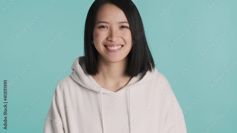Beautiful smiling Asian girl dressed in white hoodie looking cute on camera over colorful background. Joyful expression Beautiful smiling Asian girl dressed in white hoodie looking cute on camera over colorful background. Joyful expression