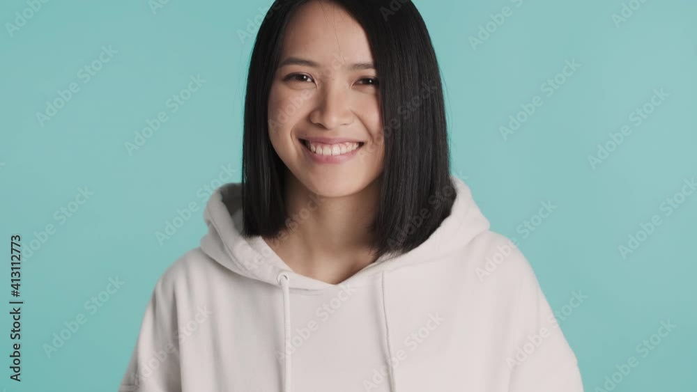 Beautiful Asian girl dressed in white hoodie looking happy over colorful background. Young stylish woman posing in studio Beautiful Asian girl dressed in white hoodie looking happy over colorful background. Young stylish woman posing in studio