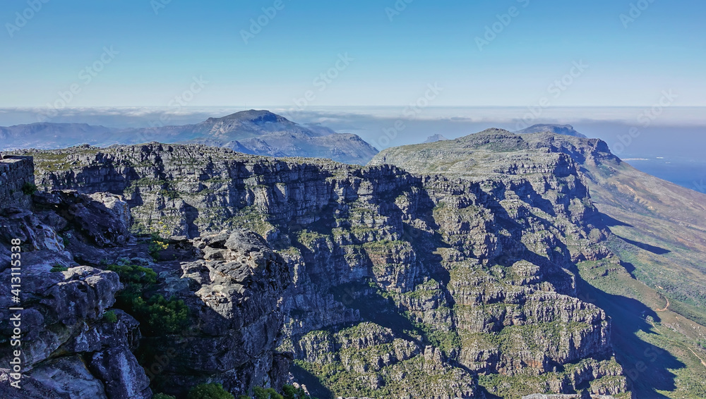 Mountain panorama from the summit of Table Mountain in Cape Town. Rocky slopes and peaks with little green vegetation. Clouds around the peaks. South Africa