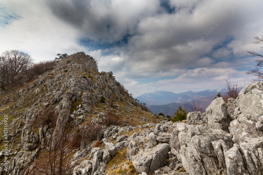 Beautiful scenery in the mountains with sharp limestome rocks, hiking path and April sky and showers, with cumulus clouds