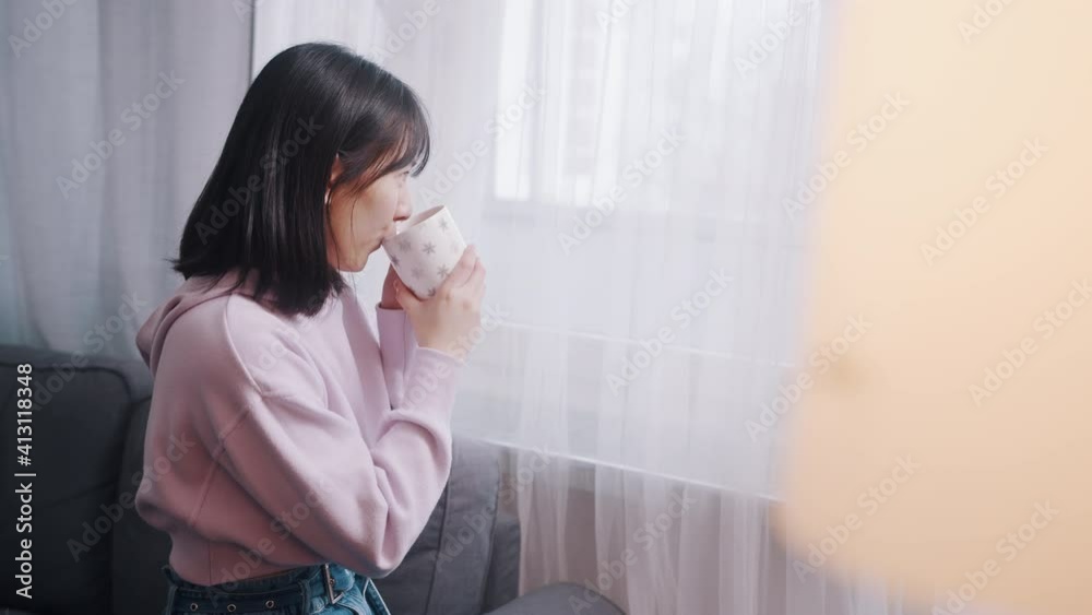 Young lonely asian woman drinking morning coffee and looking through the window. High quality 4k footage Young lonely asian woman drinking morning coffee and looking through the window. High quality 4k footage