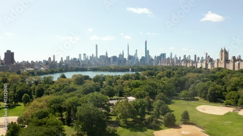 Manhattan Skyscrapers revealing behind beautiful Green Nature with Trees and Lake in Central Park, New York City, Aerial Wide View