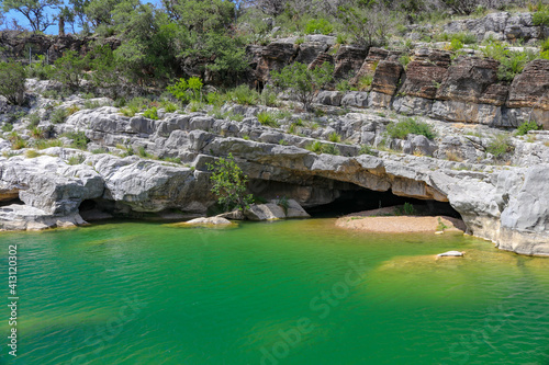 Emerald green geological rock pools of water flow into a shallow limestone canyon wall creating a smaill cave in Pedernales Falls State Park Texas 