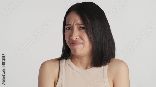 Young Asian woman feeling disgusted displeasedly looking in camera over white background. Do not like expression