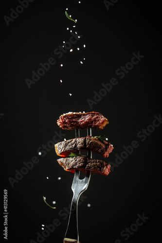 Fototapeta Naklejka Na Ścianę i Meble -  Traditional American barbecue dry aged flank steak sliced on a fork adding rosemary and sea salt in a freeze motion on black background. vertical image, American cuisine