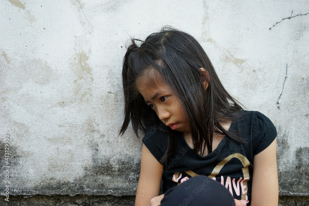 Depressed 7 years old Asian little girl sitting alone on dirty floor. Copy space. Kid with attention deficit hyperactivity disorder (ADHD), can not handle her emotion.