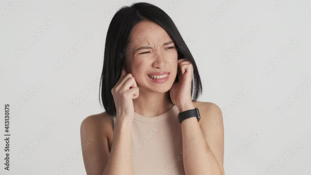 Young Asian woman covering ears with fingers because it so loud around over white background. Do not want hear it