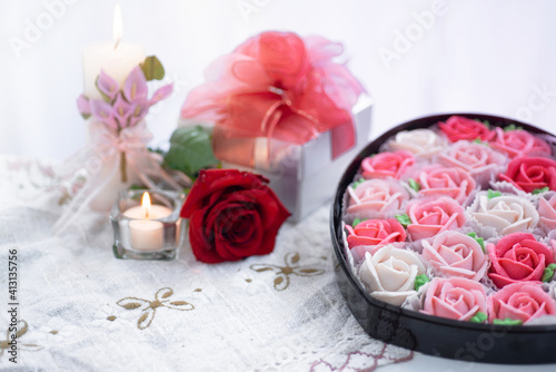 Fototapeta Naklejka Na Ścianę i Meble -  Rose shaped dessert in a heart shape box for Valentine's day, with rose flowers and candle near by , selective focus, presents for Valentine's day