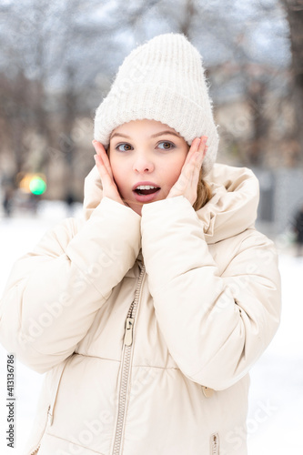 portrait of a teenage girl in winter warm clothes. the woman is surprised, her mouth is open, her hands are on her face