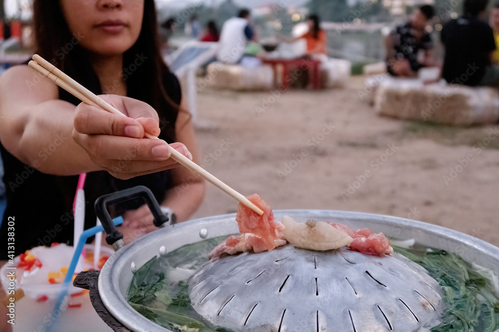 Fototapeta premium Asian woman using chopsticks to roast meat, vegetables and broth Thai is called pork pan - moo kra ta.