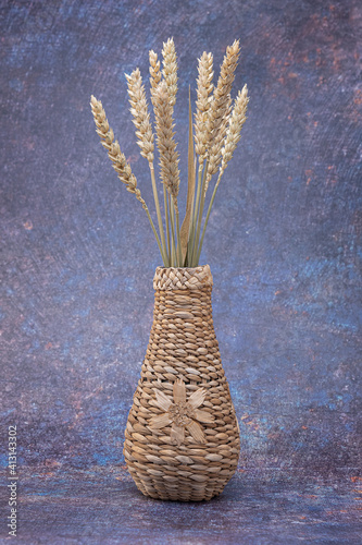 A wicker vase with a flower, with spikelets of wheat, on a dark mottled background