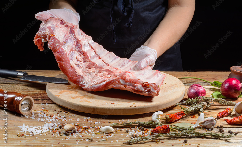 The chef uses his hands to slice pork ribs with a knife on a wooden cutting table. Selective focus. The concept of the cooking process.