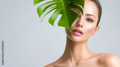 Beautiful woman with green leave near face and body. Closeup girl's face with green leave. Skin care beauty treatments concept.
