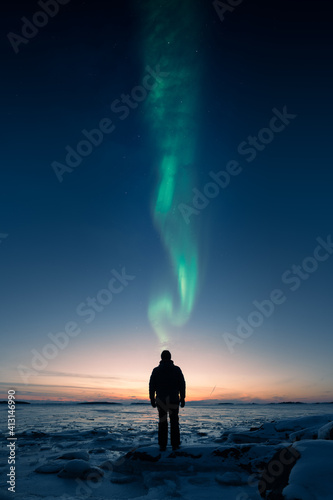 A man standing on ice an loking at sunset with Auora above his head