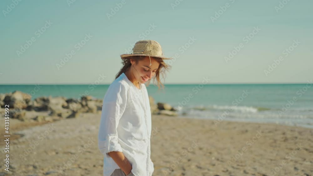 portrait of beautiful stylish woman traveler in white shirt and straw hat walking along sea coastline and enjoying sunset at seaside. portrait of beautiful stylish woman traveler in white shirt and straw hat walking along sea coastline and enjoying sunset at seaside.