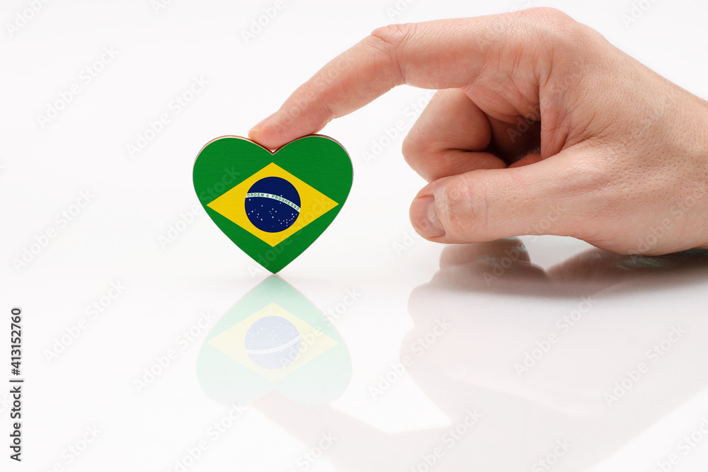 Love and respect Brazil. A man's hand holds a heart in the shape of the Brazil flag on a white glass surface. The concept of Brazilian patriotism and pride.