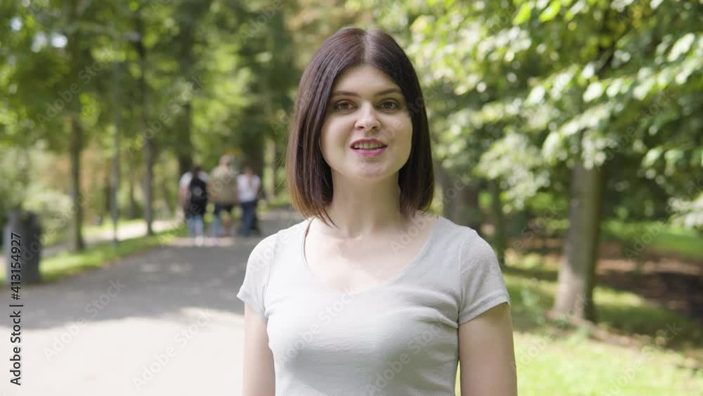 A young Caucasian woman talks to the camera on a pathway in a park on a sunny day A young Caucasian woman talks to the camera on a pathway in a park on a sunny day