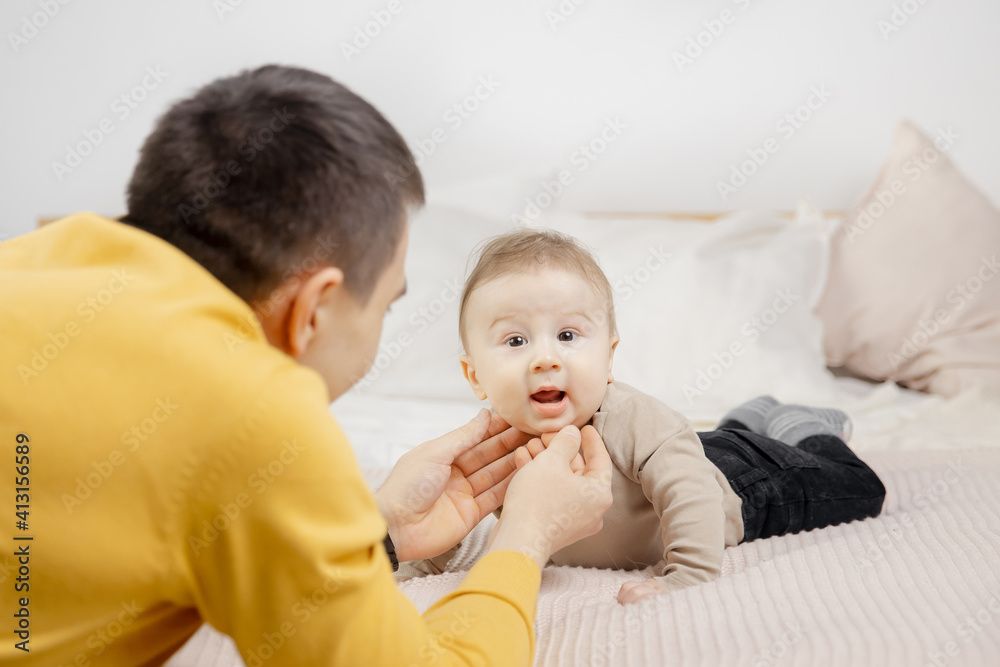 Father man trains newborn son on bed white color Father man trains newborn son on bed white color
