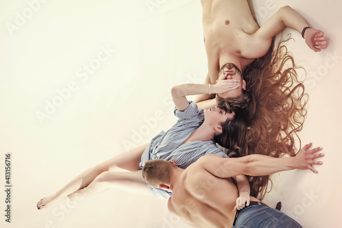 Threesome. Sexy evening for young couple and sex protection. Safety sex concept. Erotic, desire concept. Girl with long hair lie on back with legs raised. Relationship, love and romance