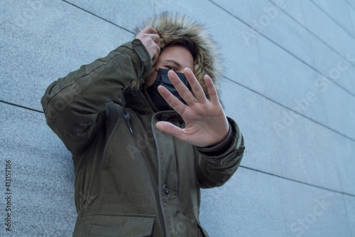 young man with a medical mask on his face protecting himself against viruses and infections and with his hand in front of the camera lens in an attitude of denial or stop photo