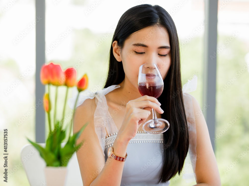 A beautiful young cute black long hair Asian woman sitting in a restaurant holding and smelling red wine in the glass A beautiful young cute black long hair Asian woman sitting in a restaurant holding and smelling red wine in the glass