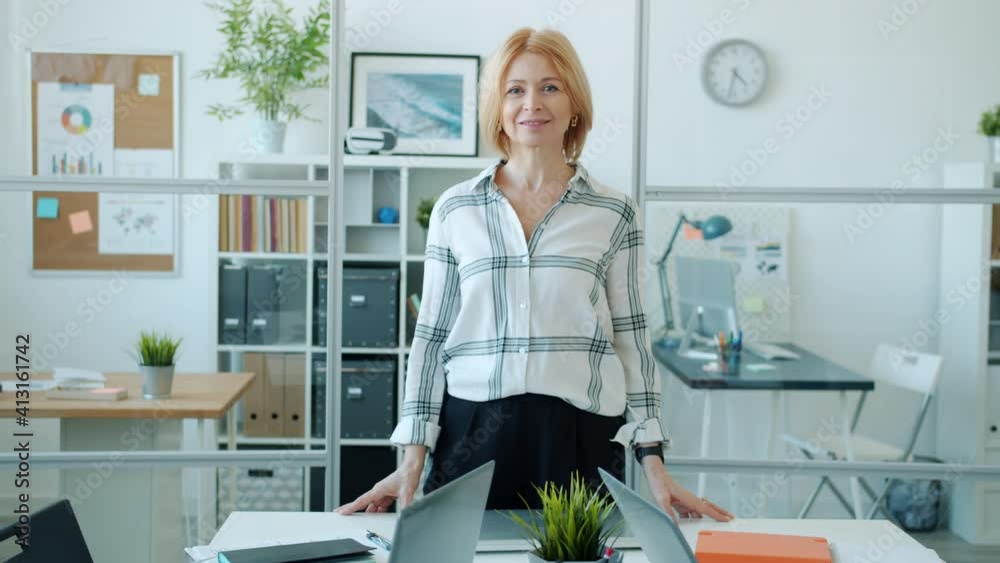 Portrait of successful mature business lady standing in office with happy smile looking at camera alone. Positive emotions and modern workplace concept. Portrait of successful mature business lady standing in office with happy smile looking at camera alone. Positive emotions and modern workplace concept.
