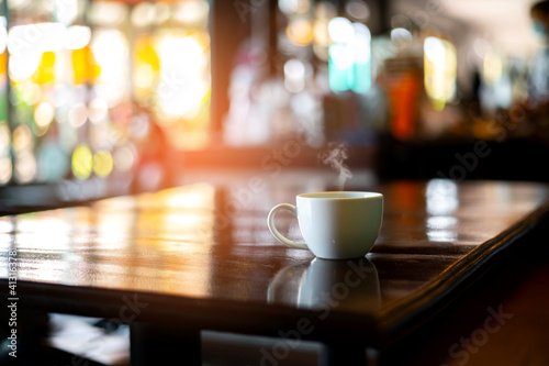 White hot coffee cup with steam on the table in blurred cafe background.Photo select focus.